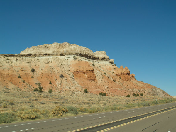 Figure 3: Colorado Plateau: Cliff along Highway 550 near San Ysidro, New Mexico. The colorful rock layers are flat-layered Mesozoic Era rocks from the age of dinosaurs. From bottom to top are Triassic Period rocks in the valley, with Jurassic Period sandstone, limestone, and gypsum above. They are topped in some places with Cretaceous Period rocks. Photograph by Jayne C. Aubele, New Mexico Museum of Natural History and Science.
