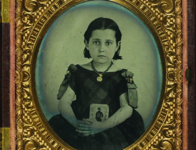 Unidentified girl in mourning dress, ca. 1861–1870. The girl holds a framed photograph of her father. Judging from her necklace, mourning ribbons, and dress, it is likely that her father was killed in the war. Courtesy of the Library of Congress.