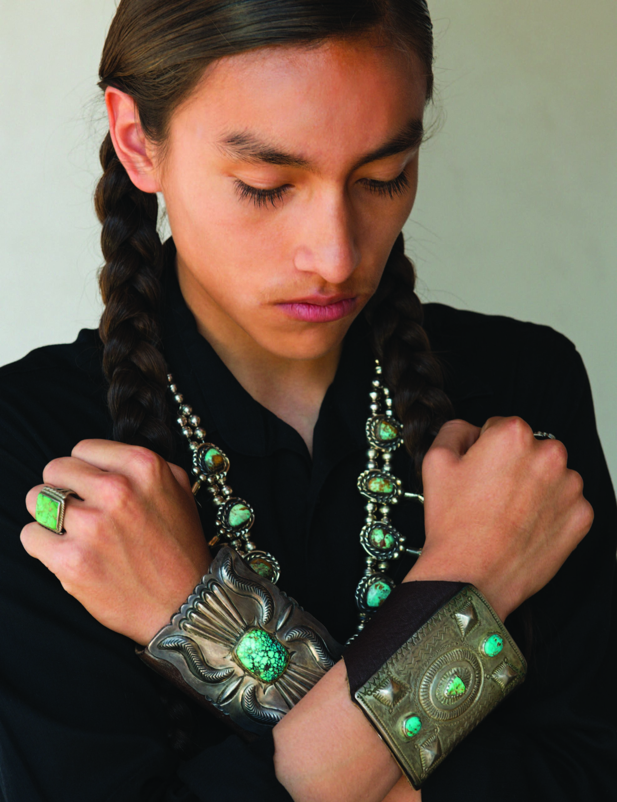 Phillip NoiseCat, with pieces from the exhibition. Large squash-blossom necklaces are often worn by men, as are ketohs (bow guards), which historically protected archers from string spring-back but today are considered jewelry items akin to bracelets. The ketoh with the square cabochon, made by Luther Aguilar, Santo Domingo, features a wonderful turquoise stone with “spiderweb” style matrix. The ketoh with three stones is Navajo, donated in 1939. Photo by Kitty Leaken.