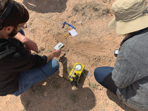 Visitors conduct a search for the hottest radioactive “hot spot” at Trinity Site. Using a digital radiation detector (white), a personal dosimeter (on the lanyard) and an analog Geiger counter (yellow box), these civilians are zeroing in on a dubious treasure. The Geiger counter sounded like the hollow ticking of an irregular but agitated clock. Photograph by Andrew Wice.