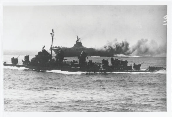 The U.S. Navy aircraft carrier USS Intrepid (CV-11) afire, after it was hit by a kamikaze off Okinawa on April 16, 1945. A Fletcher-class destroyer steams by in the foreground. Official U.S. Navy Photograph, now in the collections of the National Archives, catalog no. 80-G-328441.