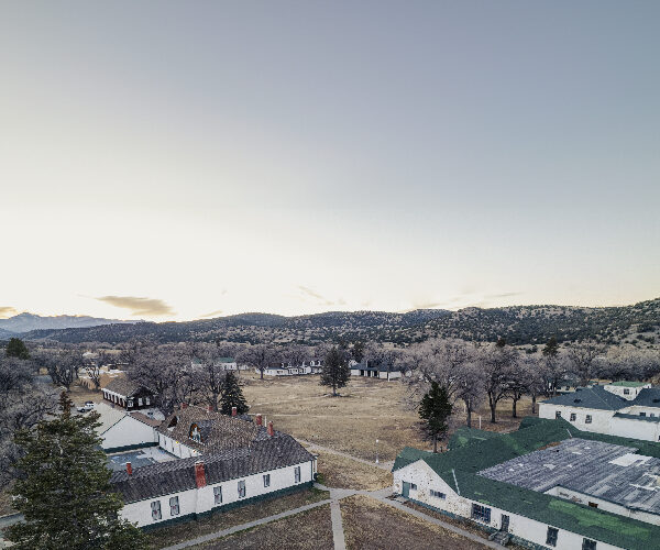 Aerial view of the Fort Stanton parade ground with the Visitor Center/ Museum on the left and the Barracks/Dining Hall on the right in the foreground. Both structures, which were originally barracks, and the parade ground date to 1855. The Sierra Blanca Mountains can be seen in the distance and are a part of the Mescalero Reservation. Photo by Tira Howard.